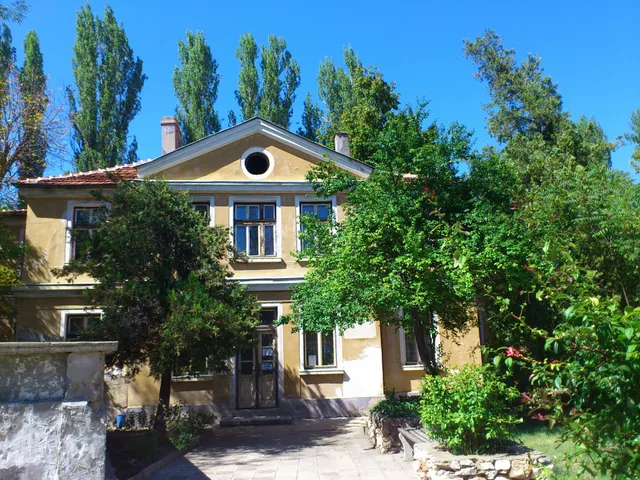 Сградата на банята откъм градината, с пейката и каменната ограда.