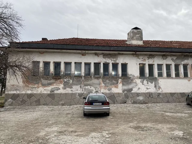 Дългата фасада на банята с олющената мазилка.